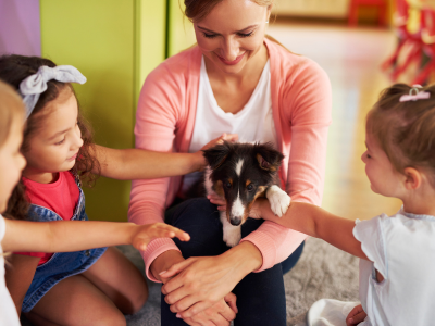 Young teacher holding a small therapy dog for a group of young students to pet. 