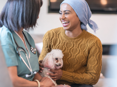 A female cancer patient laughs with her doctor while petting a therapy dog during an appointment