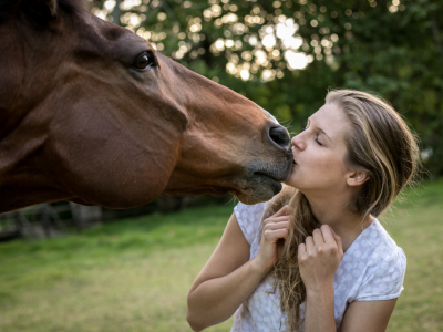 A young woman kisses a horse outdoors, illustrating the power of the human-animal bond