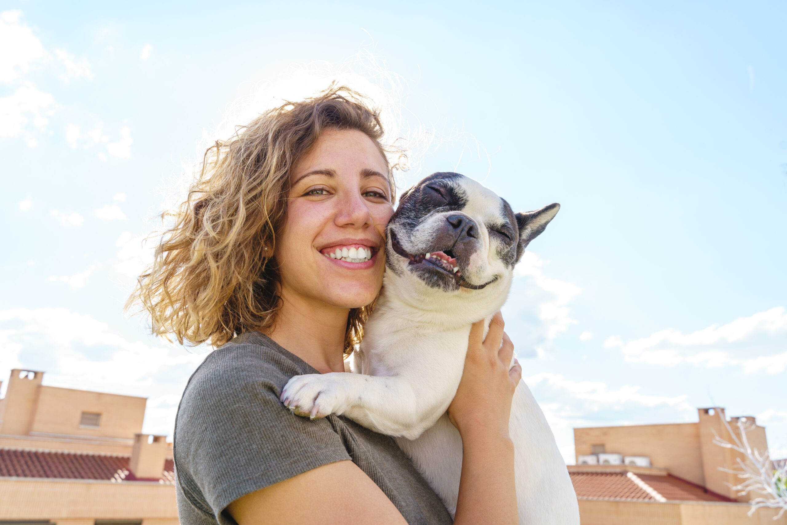 Woman holds small smiling therapy French bulldog outdoors