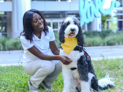 Woman smiles at therapy dog while sitting outdoors by an office building